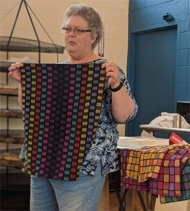 Jamie2Jamie showed us a hat she had knit with yarn she had fractal spun from painted roving, and she also brought five cotton towels she had woven in a false damask check pattern (Strickler 246). Four are in the background and she is holding her favorite.