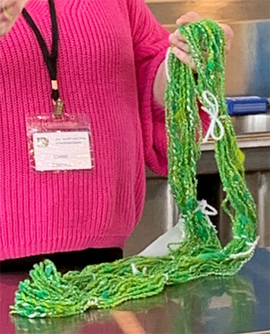 Chris's card challenged her to spin a 3 ply yarn using silk as a ply. She used her own hand-dyed wool when she spun two individual yarns in a clockwise direction. Next she plied them together in a counterclockwise direction to make a 2 ply wool yarn. For the third ply, Chris spun silk into yarn in a counterclockwise direction. Finally, to produce her very attractive cabled yarn, she spun the 2 ply wool yarn together with the single ply silk yarn in a clockwise direction