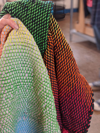 Donna wove three rugs with T-shirt wefts seen in the photo on the left. In the photo on the right is a closeup of the two that had painted rainbow warps; one has gray T-shirts for weft, the other has black T-shirts for weft.
