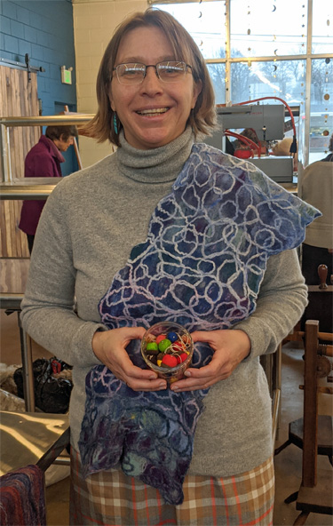 Tonya us wearing one of her attractive felted lace scarves and holding a container of cute felted acorn ornaments. 